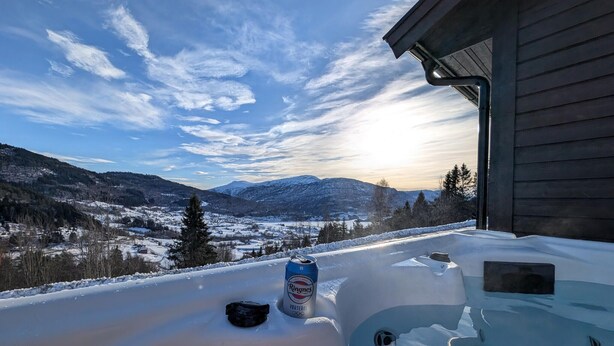 Ett snötäckt utomhusområde med en ölburk, ett svart föremål och en träbyggnad i bakgrunden.