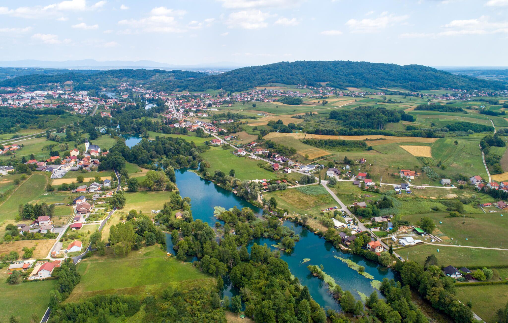 An aerial view of a town with a river, surrounded by green fields and hills.
