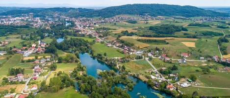 An aerial view of a town with a river, surrounded by green fields and hills.