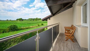 Un balcón con vistas a un campo verde, una mesa y sillas de madera y una barandilla de metal.