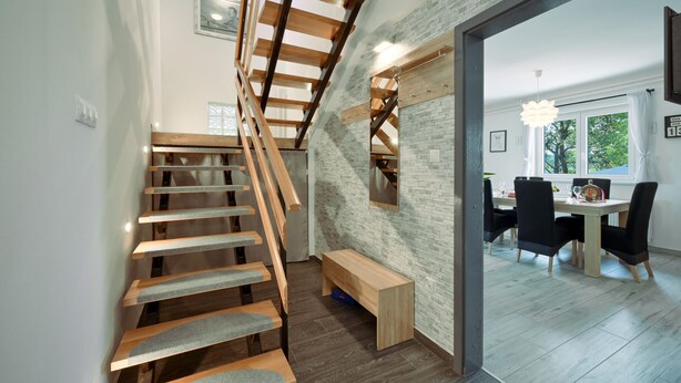 Una escalera moderna con peldaños de madera y barandilla de metal, que conduce a un comedor con mesa y sillas.