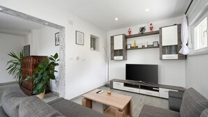 Una sala de estar moderna con un sofá gris, una mesa de centro de madera, un televisor de pantalla plana y una decoración minimalista.