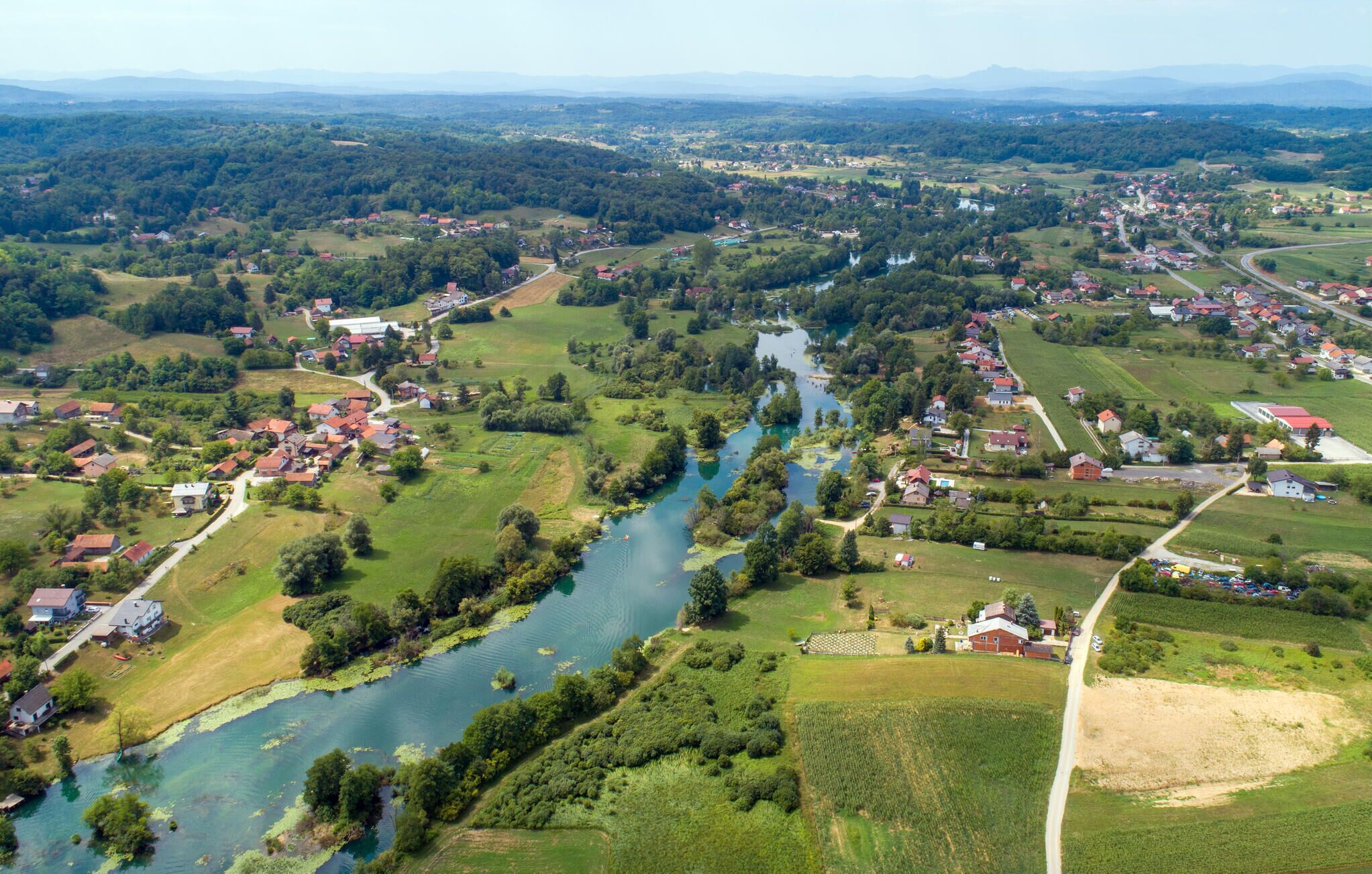 An aerial view of a rural landscape with a river, houses, and fields.