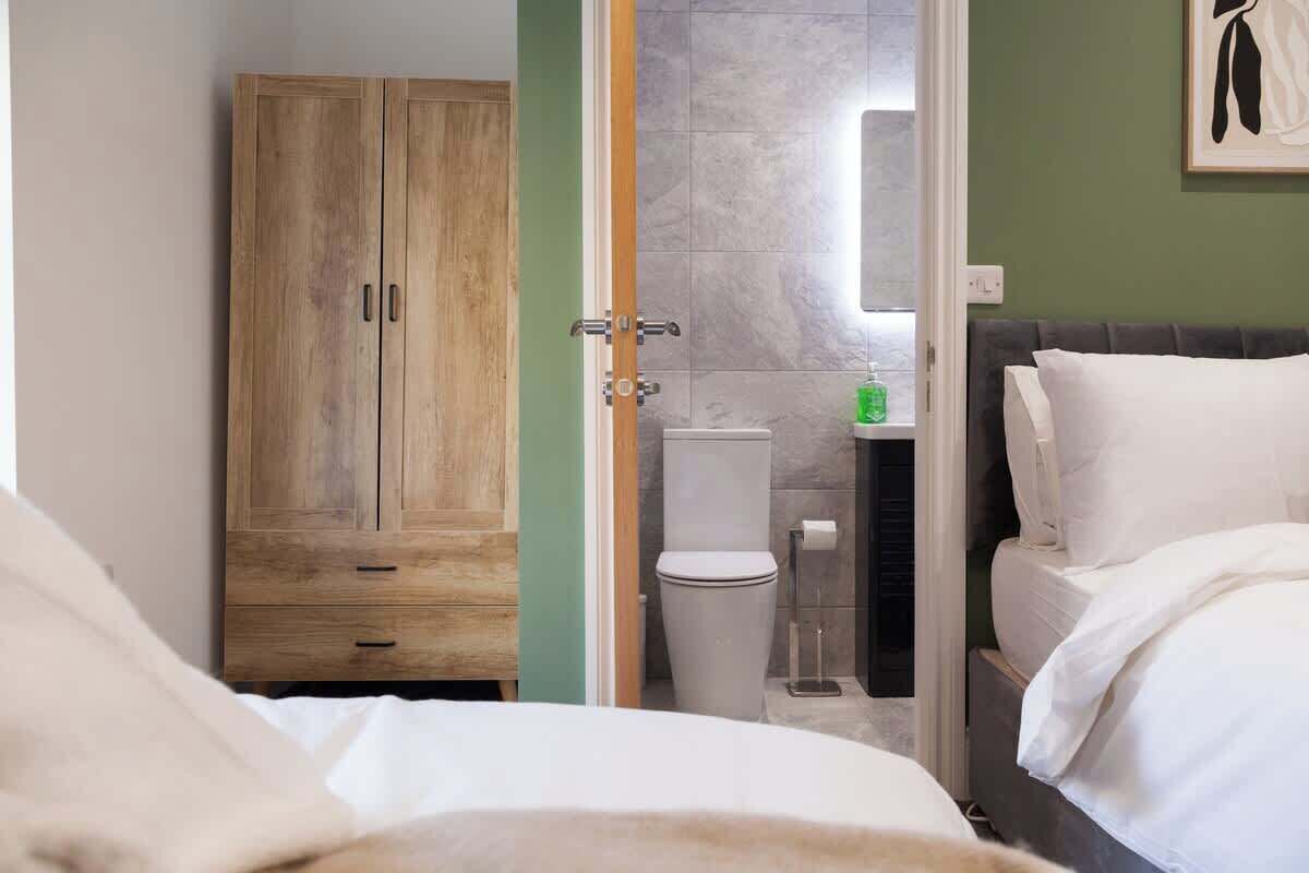 A bedroom with a bed, a wooden wardrobe, a toilet, and a small bathroom area.