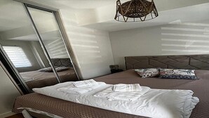 A neatly made bed with a headboard, a large mirror, and a hanging light fixture.