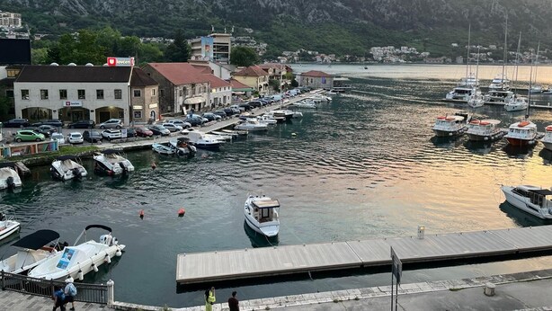 A marina with boats docked, a dock, and buildings in the background.
