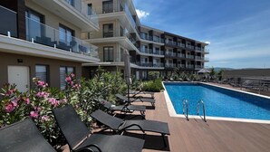 Un área de piscina en la azotea con sillones de descanso y una piscina azul cristalina.