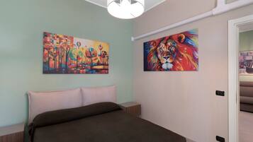Een slaapkamer met een bed, twee schilderijen, een witte plafondlamp en een deur naar een andere kamer.