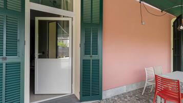 Una habitación con puerta blanca, contraventanas verdes, pared rosa y una mesa con dos sillas.