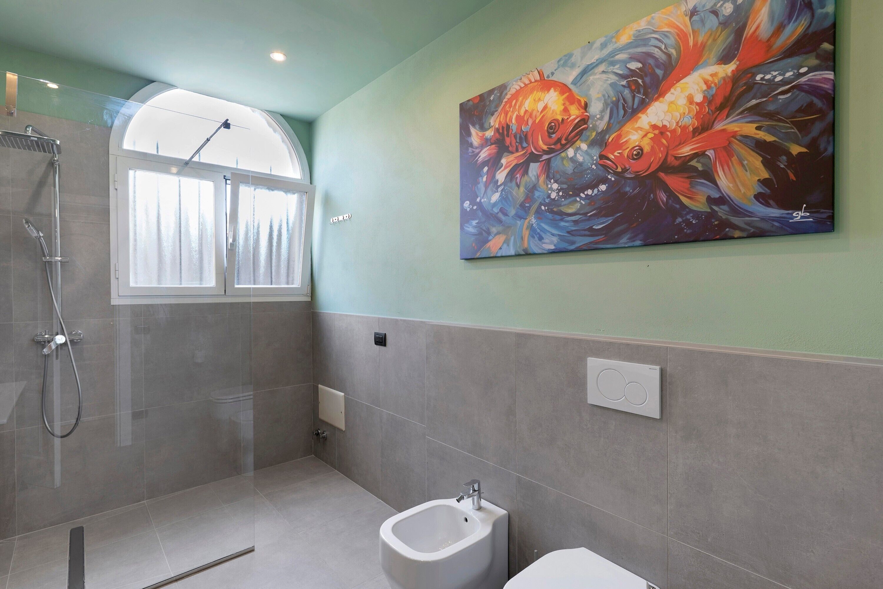 A bathroom with a shower, bidet, and a painting of fish on the wall.