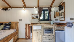 A compact kitchen with wooden cabinetry, a built-in oven, and a small refrigerator. - Tanglewood Shepherds Hut (Welshpool)