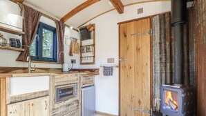A rustic kitchen with wooden cabinets, a built-in oven, a stove, and a window with curtains. - Tanglewood Shepherds Hut (Welshpool)