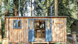 A wooden cabin with a blue door and windows, a chimney, and a small porch area with potted plants. - Tanglewood Shepherds Hut (Welshpool)