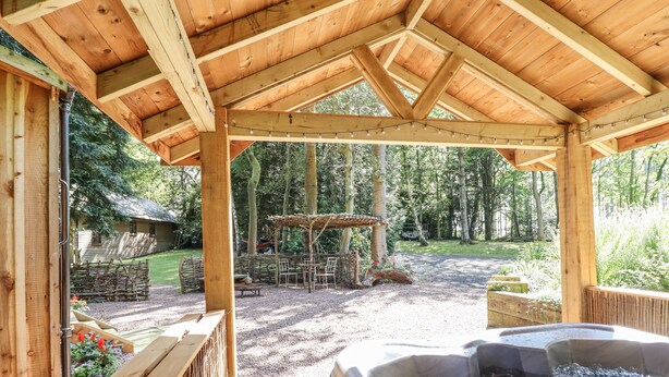 A wooden gazebo with a hot tub and outdoor seating area. - Tanglewood Shepherds Hut (Welshpool)