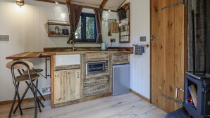 A rustic kitchen with wooden cabinets, a built-in oven, a microwave, and a wood-burning stove. - Tanglewood Shepherds Hut (Welshpool)