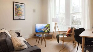 Una sala moderna con sofá, televisor, una mesita y zona de comedor.