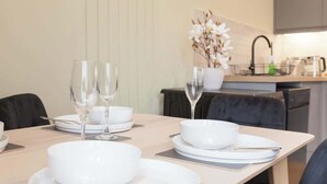 Una mesa de comedor con platos, tazones y copas de vino blancos, con una cocina moderna al fondo.