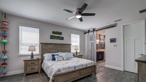 Une chambre à coucher avec un lit en bois, deux tables de chevet, un ventilateur de plafond et un tapis orné de motifs d’étoiles de mer.