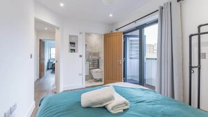 A modern bedroom with a large bed, a sliding glass door to a balcony, and a view of the city.