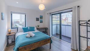 A modern bedroom with a bed, bedside table, and a view of the city through a large window.