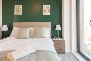 A neatly made bed with white linens, two bedside lamps, and a window with a view of the outside. - 3 Bed Flats near Station & City Centre - Sleeps 6 (Leeds)
