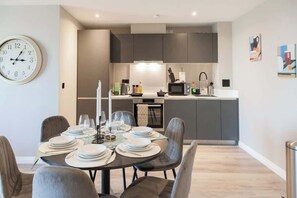 A modern kitchen with dark cabinets, a microwave, and a sink. There is a dining area with a table set for four, including plates, glasses, and cutlery. - 3 Bed Flats near Station & City Centre - Sleeps 6 (Leeds)