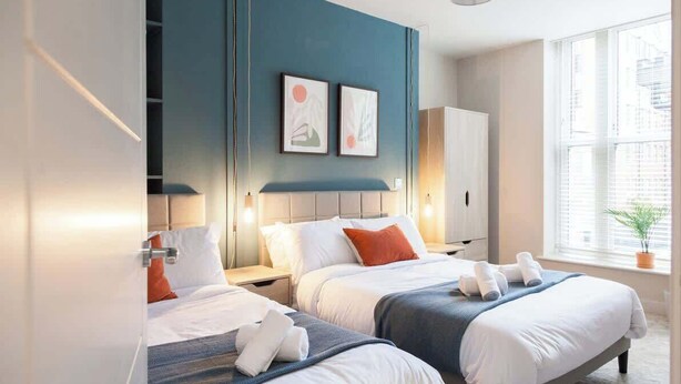 Une chambre d’hôtel avec deux lits, une grande fenêtre avec des stores et des œuvres d’art accrochées au mur.
