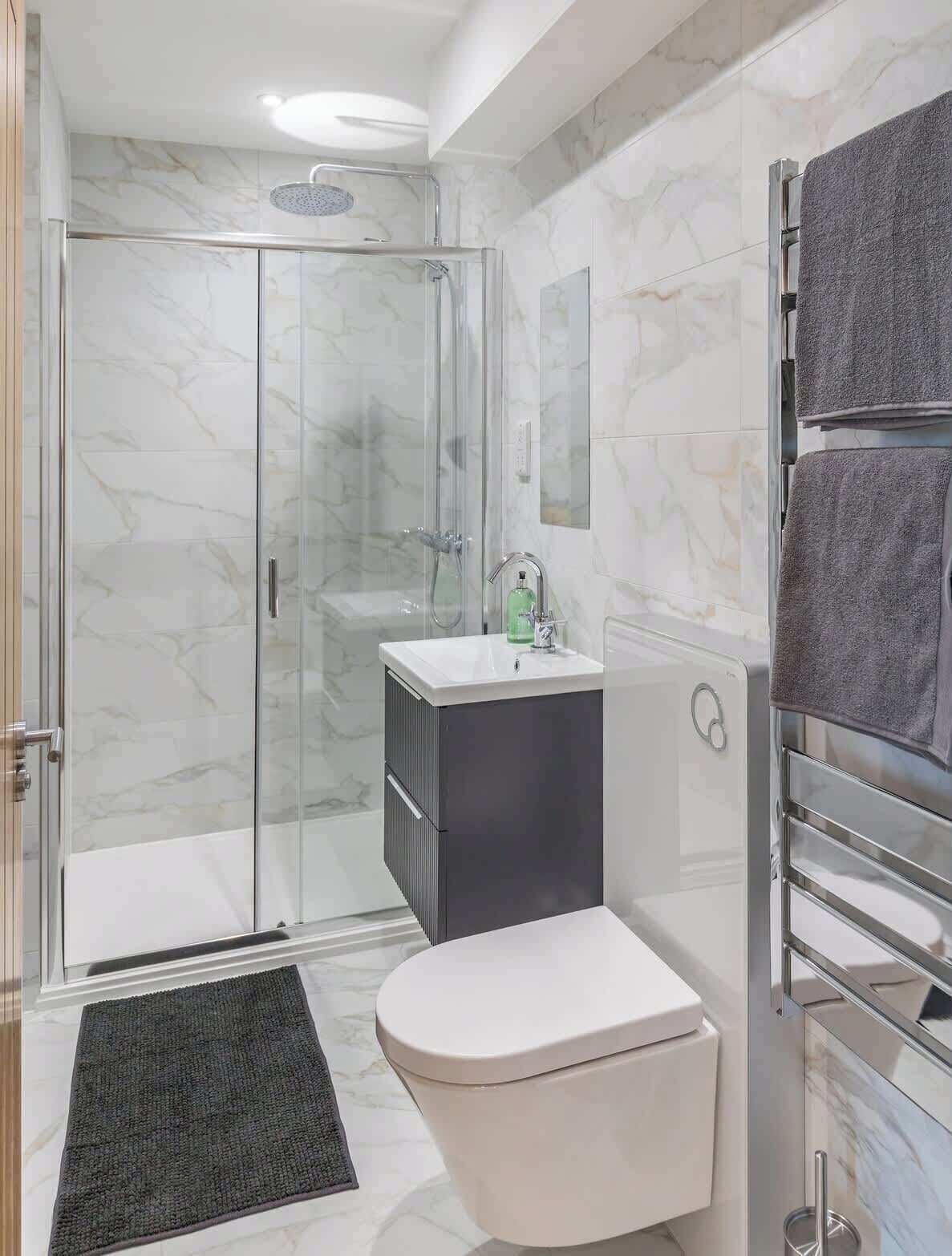 A modern bathroom with a glass-enclosed shower, a white toilet, a dark cabinet, and a towel rack with two towels.