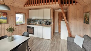 A cozy cabin-style room with a wooden interior, a dining area with a table and chairs, a kitchen with white cabinets and a tiled backsplash, and a staircase leading to an upper level. - 6 Person Holiday Park Home in Bryrup (Bryrup)