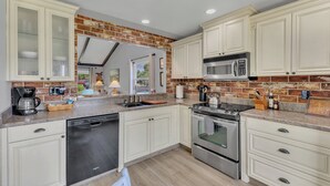 Een moderne keuken met witte kasten, een backsplash van baksteen, roestvrijstalen apparatuur en uitzicht op de omgeving.