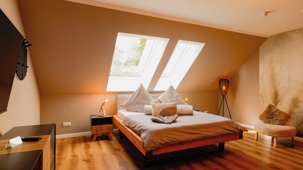 A bedroom with a large bed, two windows, a bedside table, a chair, and a desk.