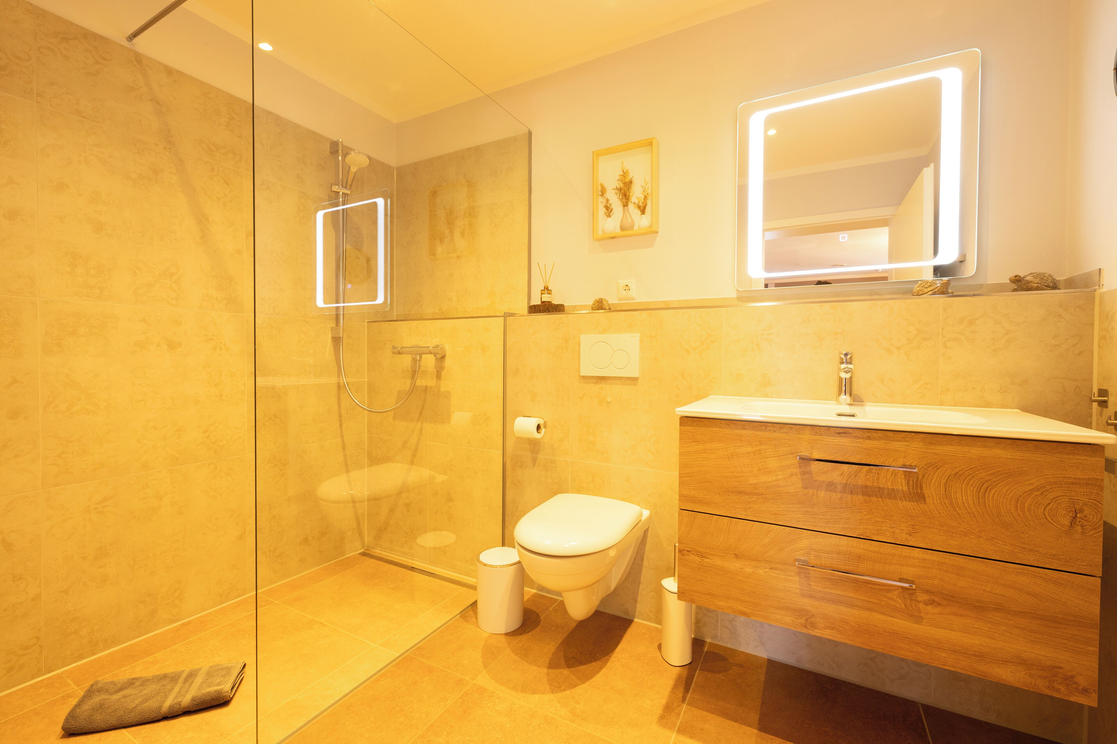 Een moderne badkamer met een douchecabine van glas, een wit toilet en een houten wastafelmeubel met spiegel.