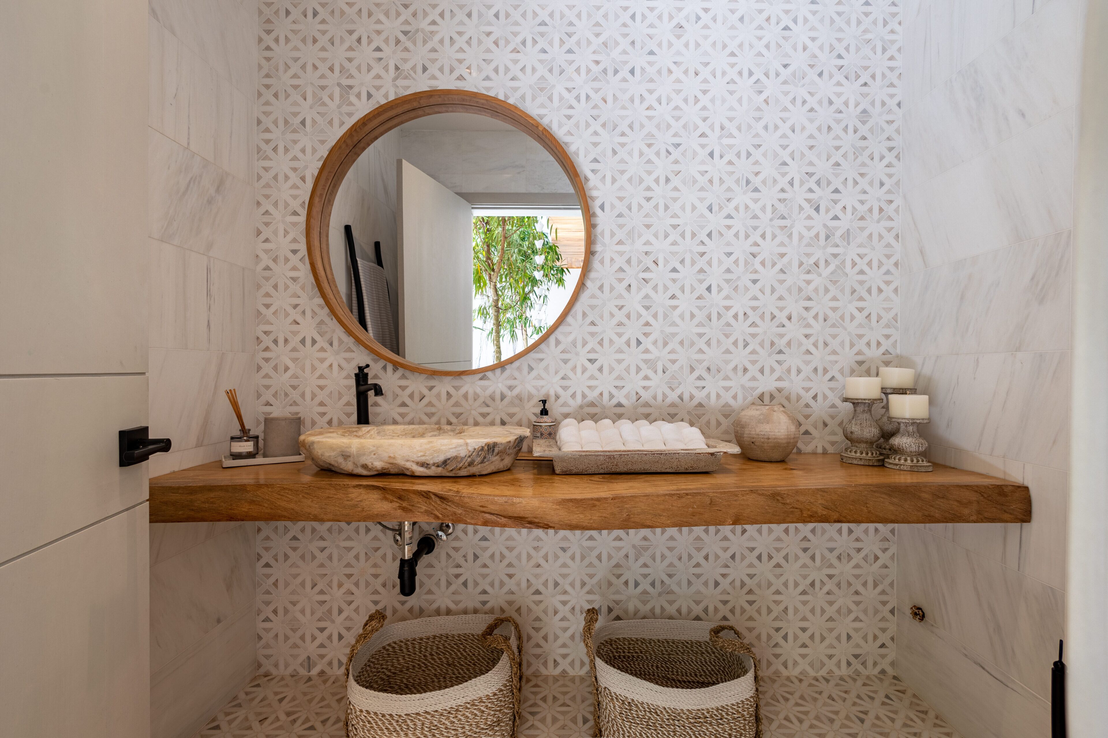 Une salle de bain avec un meuble-lavabo en bois, un miroir rond et deux paniers en osier.