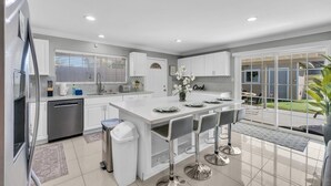 Een moderne keuken met een centraal eiland, barkrukken en uitzicht op de achtertuin.