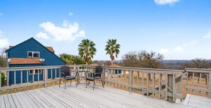 A wooden deck with a railing, a blue house, and two palm trees in the background.