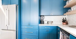 Una cocina moderna con armarios azules, un refrigerador blanco, una licuadora, un tostador y un juego de cuchillos.