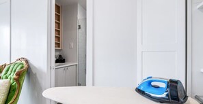 A neatly organized room with a white ironing board, a blue iron, and a green cushion on a chair.