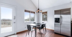 A modern kitchen with a dining table, chairs, a refrigerator, and a chandelier.