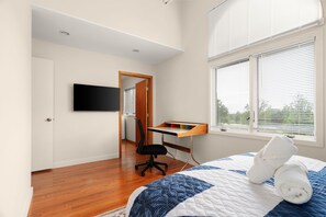 Un dormitorio con cama, escritorio, silla, televisión y ventana con persianas.
