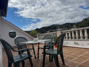 Una terraza con mesa y sillas, una planta en maceta y vistas a un paisaje montañoso.