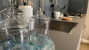 Et køkken med en stålvask, komfur og glasbeholdere på bordet.