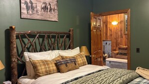 A bedroom with a wooden headboard, a bed with plaid bedding, a nightstand with a lamp, and a painting of horses on the wall. - Charming Cabin on horse farm minutes from Letchworth State park (Nunda)