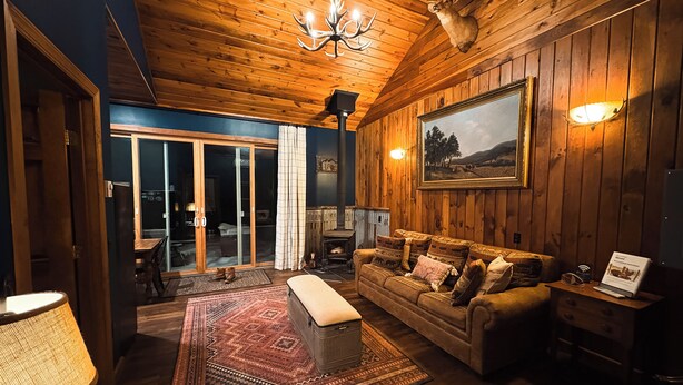 A cozy living room with a wooden ceiling, a large couch, a rug, and a fireplace. - Charming Cabin on horse farm minutes from Letchworth State park (Nunda)