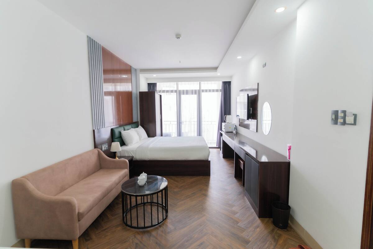 Une chambre d’hôtel moderne, équipée d’un lit, d’un canapé, d’une petite table ronde, d’un bureau et d’une grande fenêtre.