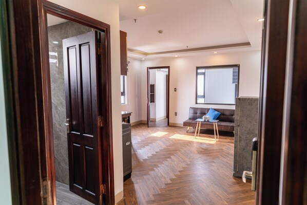 Un interior moderno con suelo de madera tipo espiga, una puerta de madera oscura, una zona de estar con sofá y una mesa de centro, y un espejo grande en la pared.