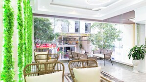 A modern indoor seating area with wicker chairs and a glass wall offering a view of a building with a sign. - MaMa Hotel And Apartment (Da Nang)