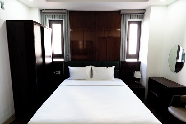 A hotel room with a large bed, dark wooden headboard, two bedside tables with lamps, and a wardrobe. - MaMa Hotel And Apartment (Da Nang)