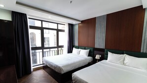 Habitación de hotel con dos camas, un ventanal con cortinas y vistas a edificios.