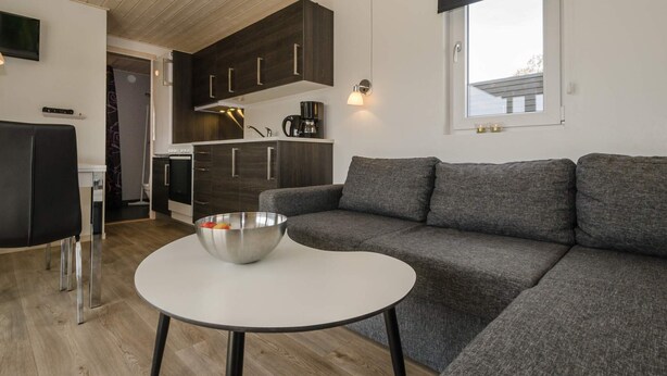 Un salon moderne avec un canapé gris, une table basse blanche et une cuisine en arrière-plan.