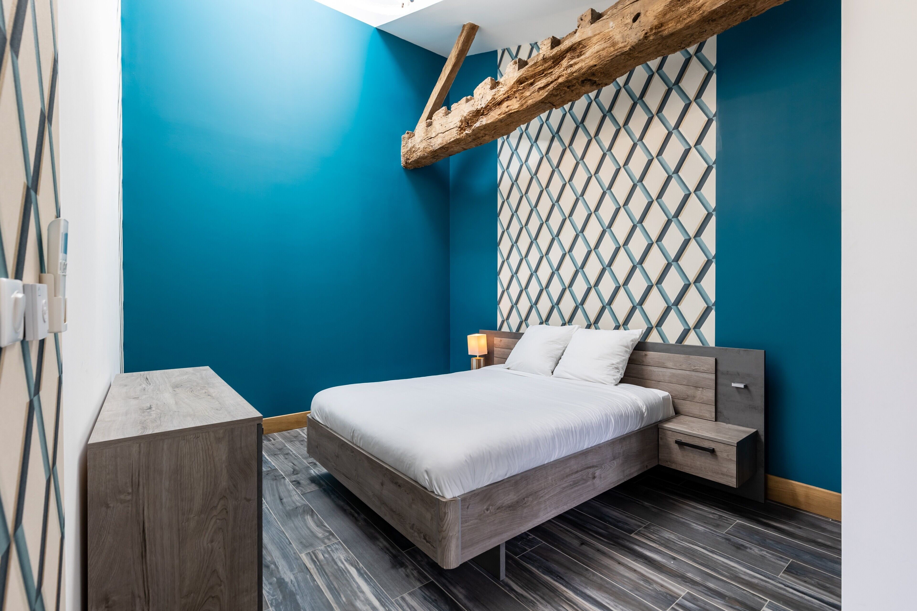 A modern bedroom with a bed, bedside tables, and a unique geometric wall pattern.